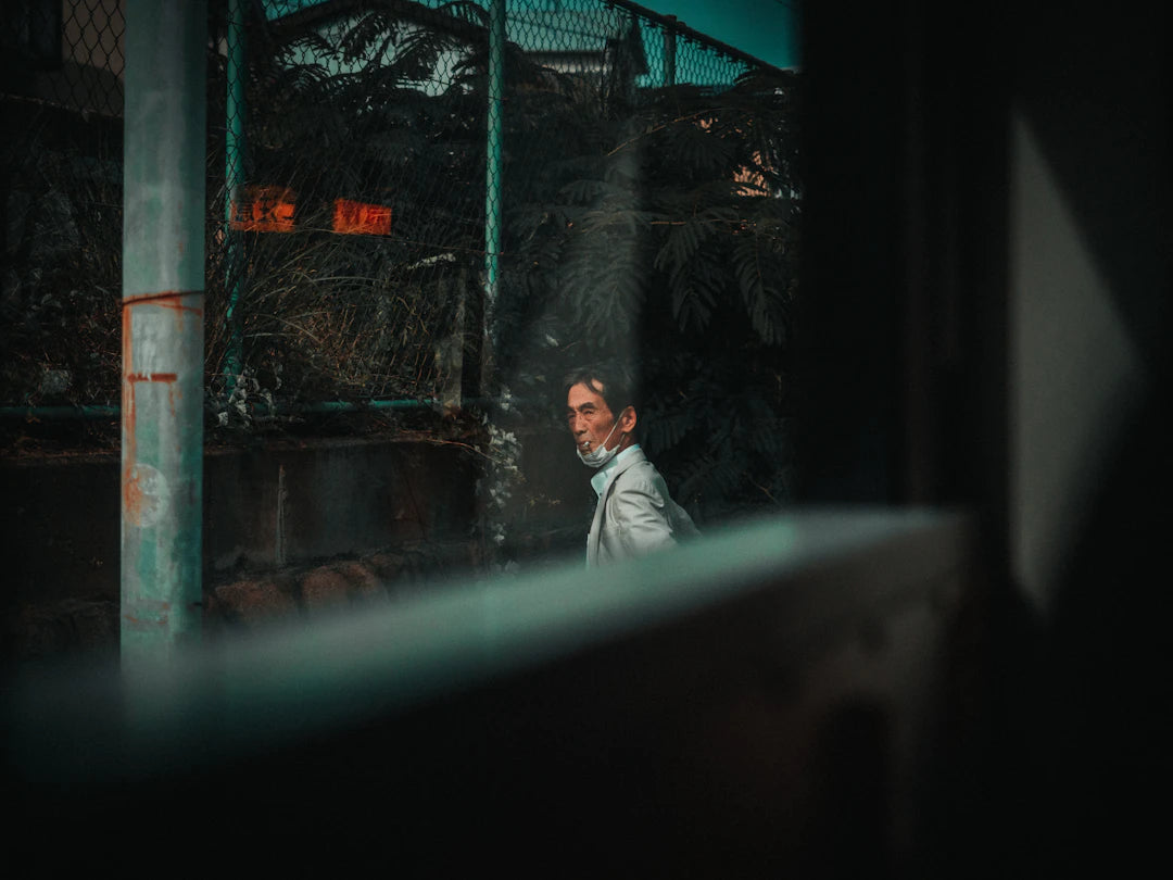 man in white dress shirt standing near green metal fence during daytime