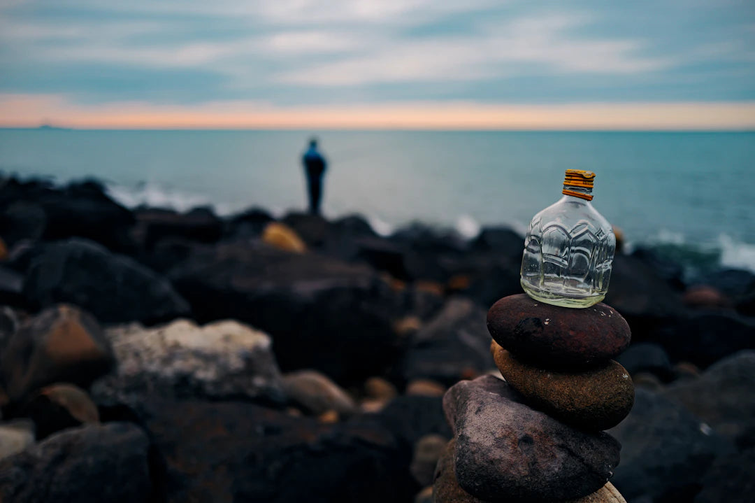 Stack of stones with bottle on rocky shore near ocean.